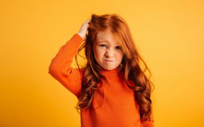 Photo of confused little redhead girl with freckles standing isolated over yellow background. Looking camera.